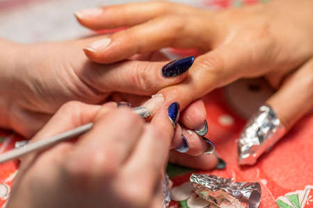 Close-up of the hands of a qualified manicurist filing the nails of a young woman.の写真素材