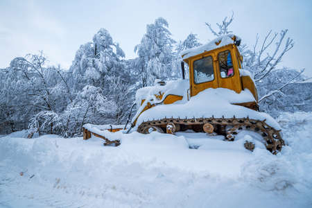 Crawler Tractor grader cleans snow on a forest road. Winter background.の写真素材