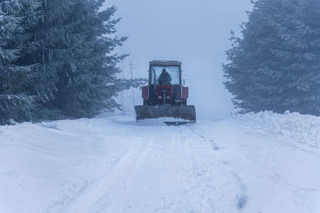 Red snowblower grader clears snow covered ski resort road in mountains or city street. Winter...