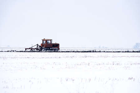 Crawler Tractor plowing field in winter.の写真素材