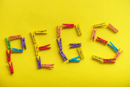 Colorful wooden clothes pegs on yellow background.の写真素材
