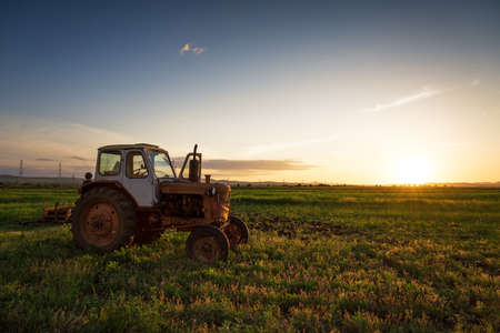Farmer plowing stubble field with red tractor at sunset.の写真素材