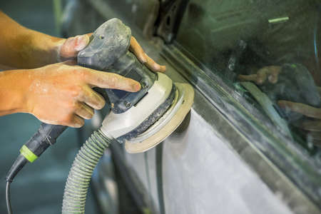 Grinder in the hands of a man who sharpen a car varnish in the car shop.