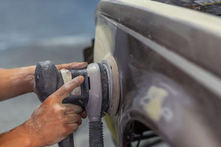 Grinder in the hands of a man who sharpen a car varnish in the car shop.