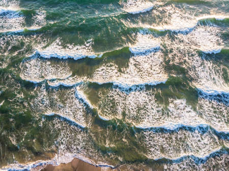 Aerial view of crashing wave in ocean with warm sunset light. Top view