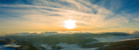 View of a winter landscape. Snow covered forest. Dramatic gold sunset sky.