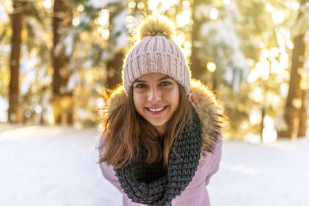 Close-up portrait of beautiful young woman in winter forest on sunset.
