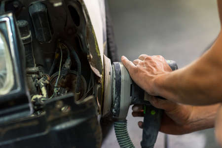 Grinder in the hands of a man who sharpen a car varnish in the car shop.