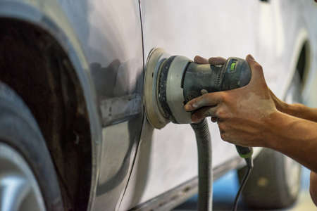 Grinder in the hands of a man who sharpen a car varnish in the car shop.