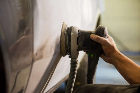Grinder in the hands of a man who sharpen a car varnish in the car shop.