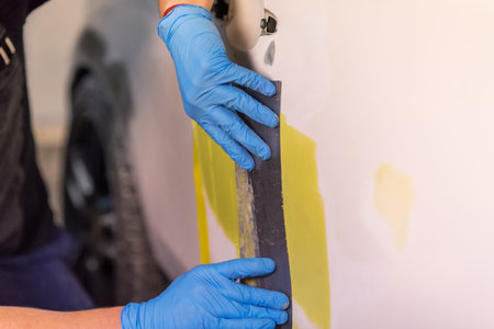 Preparation for painting a car element using emery sender by a service technician leveling out before applying a primer after damage to a part of the body in an accident in the vehicle workshop.の写真素材