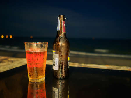 Bottle and grass of beer on the table at the beach during night time.の写真素材
