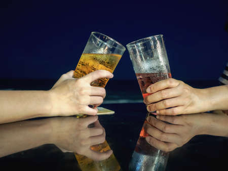 Cheers beer alcohol celebration making a toast at the beach during night time.の写真素材