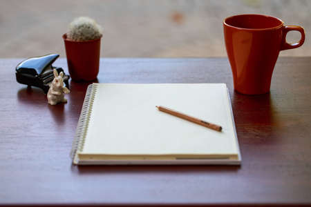 A notebook, with pencil, cactus,cermic piano and a cup of coffee on the wooden tableの写真素材