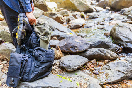 Woman hand holding backpack, hat and sandals ready to walk across the water stream, trekking and hiking concept.の写真素材