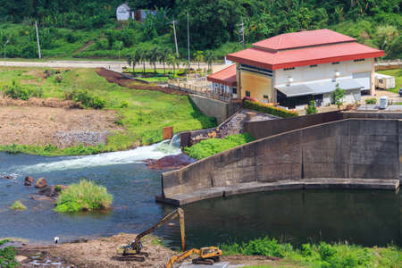 Khun Dan Prakan Chon Dam, Nakorn Nayok, Thailand â Apr 30.2017 : Water overflowing at the damâs spillway, and tracked excavator running his duty.のeditorial素材