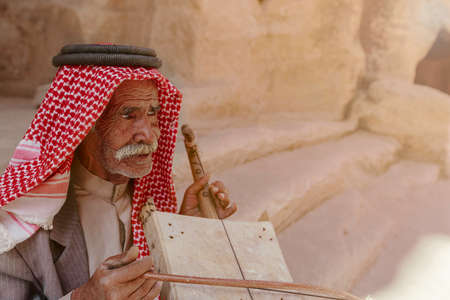 Little Petra, Jordan â June 20, 2017: Old Bedouin man or Arab man in traditional outfit, playing his musical instrument at the doorway of Little Petra.のeditorial素材