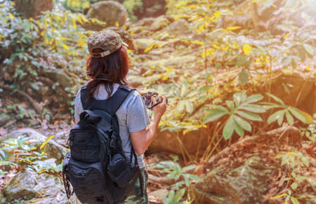 Girl with backpack and camera on trekking trip, standing alone in the trail, enjoying taking photo over the sunlight.の写真素材