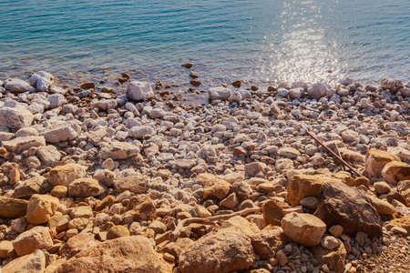 Small waves touching against salted rock shore of the Dead Sea, sun shining at the sunset time, Jordan.の写真素材