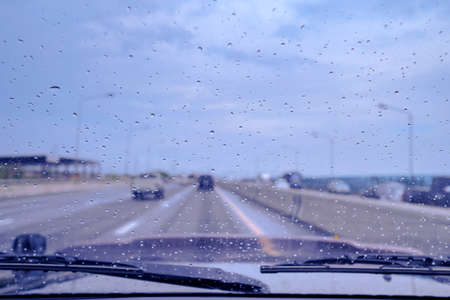 Rain drops on the car’s windscreen, raining day along the highway, cloudy sky background.