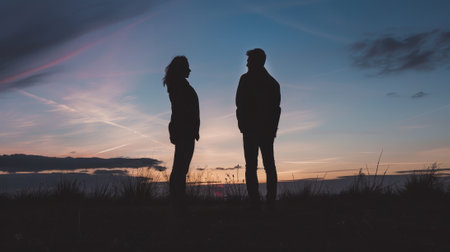 A couple standing in the grass at sunset. The man is wearing a jacket and the woman is wearing a sweaterの素材