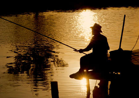 Fisherman at sunset holding his pole on dockの写真素材
