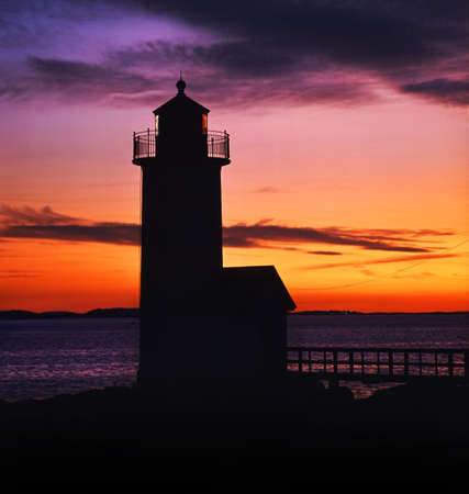 lighthouse at dusk back lit by colouful sky with purple,orange and red の写真素材