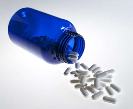 Prescription medicine pills pouring out of blue bottle on white background の写真素材