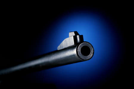 Gun barrel on black background at angle back lit by blue spotの写真素材