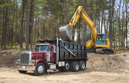 Excavator loading dumper truck with dirt at construction site の写真素材