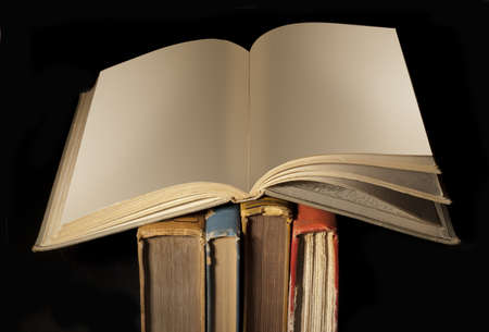 Blank open book on top of old worn spines on blackの写真素材