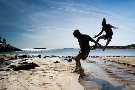 Two men jumping over a small stream  can be used as a metaphorのeditorial素材