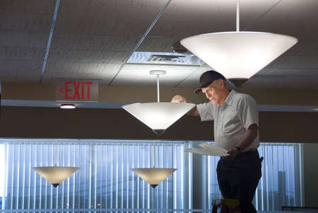 Maintenance man changing light bulbs in business officeのeditorial素材