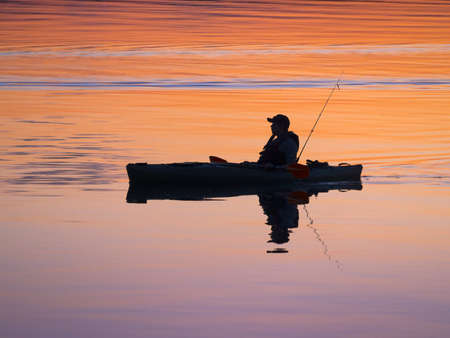 Fisherman kayaking around sunset in tranquil lakeの写真素材