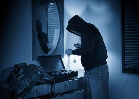 Hooded burglar ransacking a jewelry box in a homeの写真素材