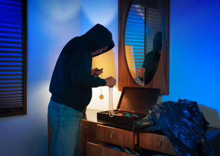 Hooded burglar ransacking a jewelry box in a homeの写真素材