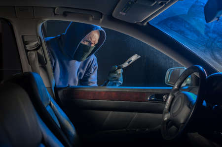 Hooded thief looking to break into a car to steal either the vehicle or objects insideの写真素材