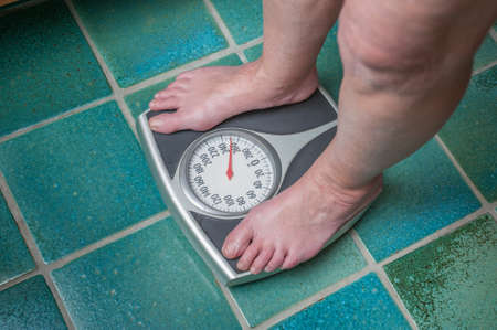 A severely overweight person weighing herself or himself on a bathroom scaleの写真素材