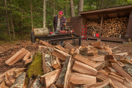 Older man using log splitter near a wood shedの写真素材