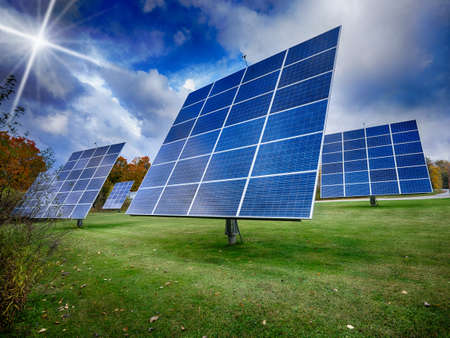 Solar panels in green field with sun shining through cloudsの写真素材