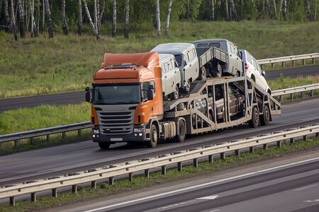 Truck for transporting cars delivers new cars on a multi-lane highway in summerの写真素材