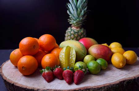 Oranges, mangos, papaya, strawberry, pineapple, limes and lemons arranged on wooden diskの写真素材