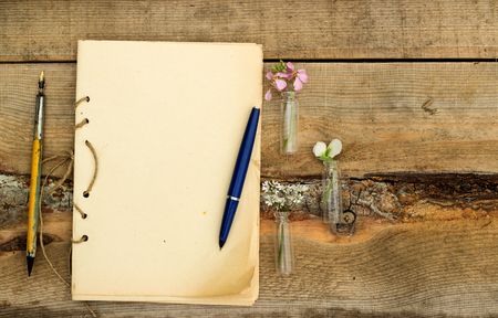 handmade sketchbook with old pen and small bouquet of wildflowers on a wooden backgroundの写真素材
