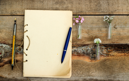 handmade sketchbook with old pen and small bouquet of wildflowers on a wooden backgroundの写真素材