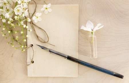 Open vintage handmade sketchbook with white bird-cherry flowers over wooden table background. Mock...