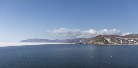 Baikal lake spring landscape view. Snow-covered shore of the lake. Rocky forested coastline. Boundary of ice and open water.の写真素材