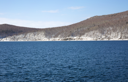 Baikal lake spring landscape view. Snow-covered shore of the lake. Rocky forested coastline.の写真素材