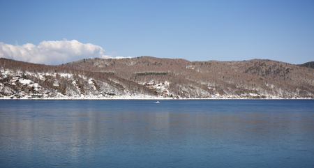 Baikal lake spring landscape view. Snow-covered shore of the lake. Rocky forested coastline.の写真素材