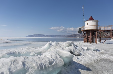 Transparent blue ice hummocks on lake Baikal shore. Siberia winter landscape view with lighthouse. Snow-covered ice of the lake. Big cracks in the ice floe.の写真素材