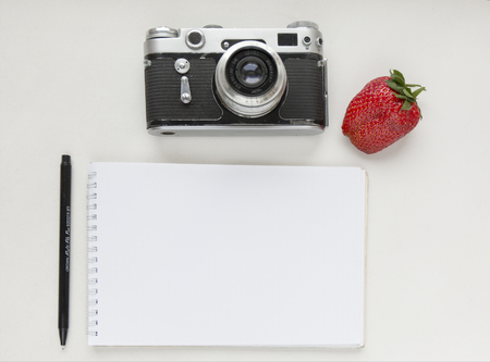 Notebook mock up for artwork with old camera, pen and red strawberries. Top view. Place for textの写真素材